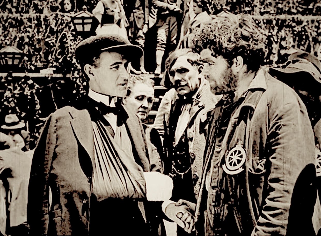 Film still: the doctor, his arm in a sling, shakes hands with a bearded mountain guide as villagers look on