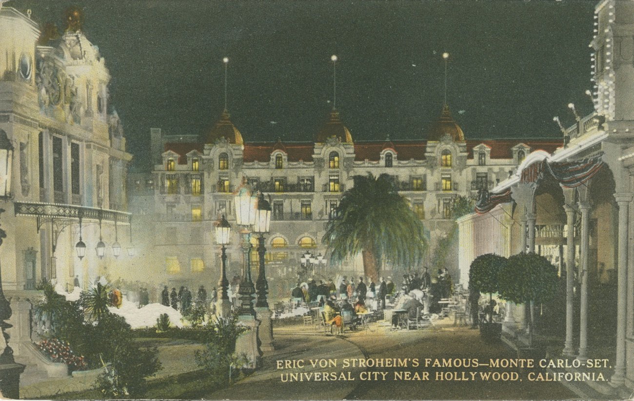 Hand-coloured 1922 postcard: the Foolish Wives Monte Carlo set lit up at night, with the casino, hotel and crowds in the plaza